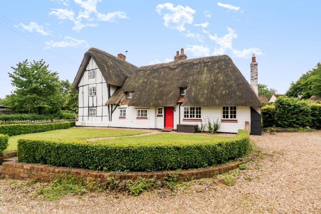 a white house with a thatched roof with a red door at Captivating 6 Bed Cottage in the village of Moulso in Newport Pagnell