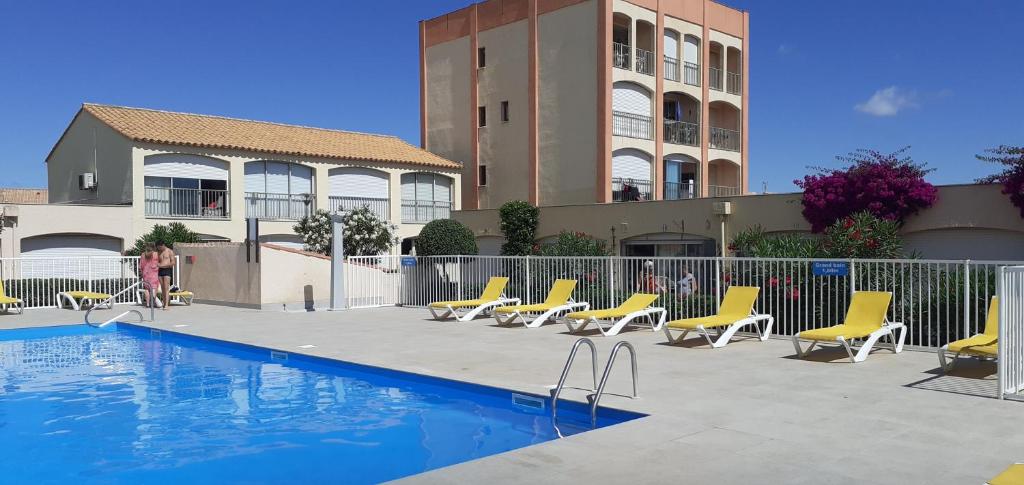 une piscine avec des chaises jaunes et un bâtiment dans l'établissement Au village cœur de Barcarès studio vue mer 3 couchages, au Barcarès