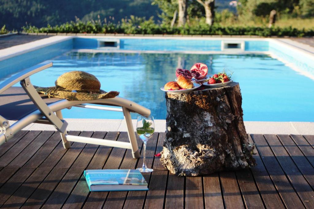 een tafel met een bord eten op een boomstronk naast een zwembad bij Casa da Choqueira in Vieira do Minho