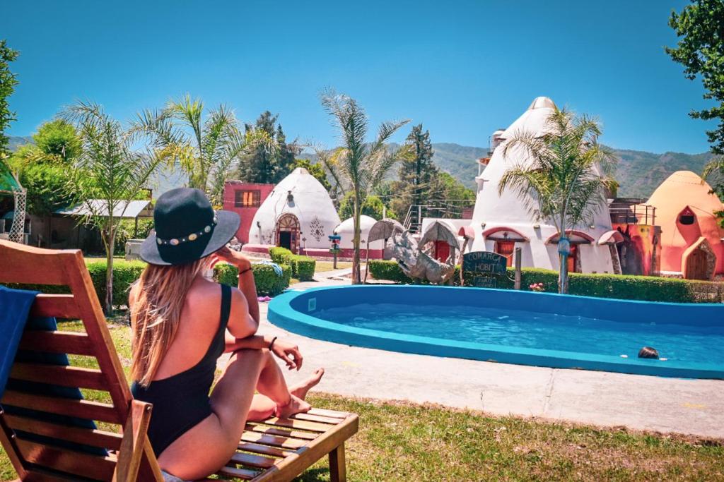 una mujer sentada en un banco junto a una piscina en Cabañas La Comarca del Hobit in 