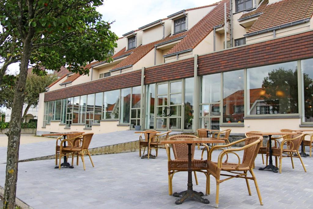 eine Terrasse mit Tischen und Stühlen vor einem Gebäude in der Unterkunft Hotel Les Dunes in De Haan