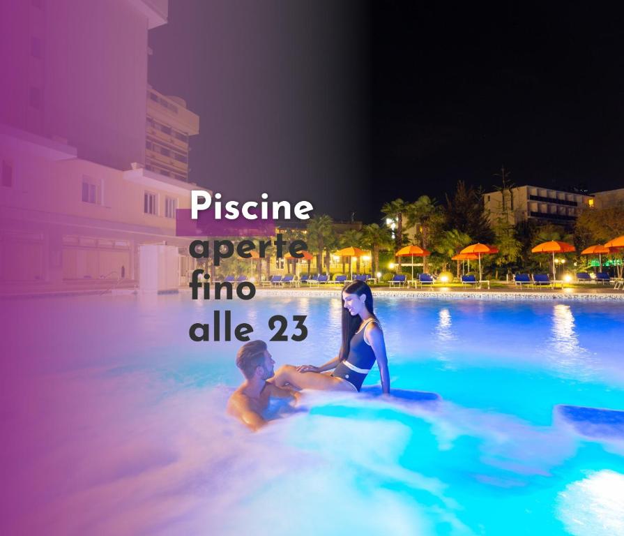two people sitting in a swimming pool at night at Hotel Savoia Thermae & SPA in Abano Terme