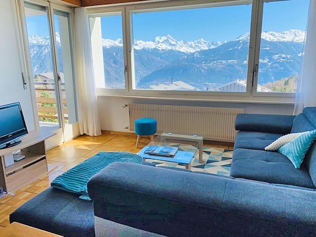 uma sala de estar com um sofá azul e uma grande janela em Apartment Grand Large A-B-1 by Interhome em Crans-Montana