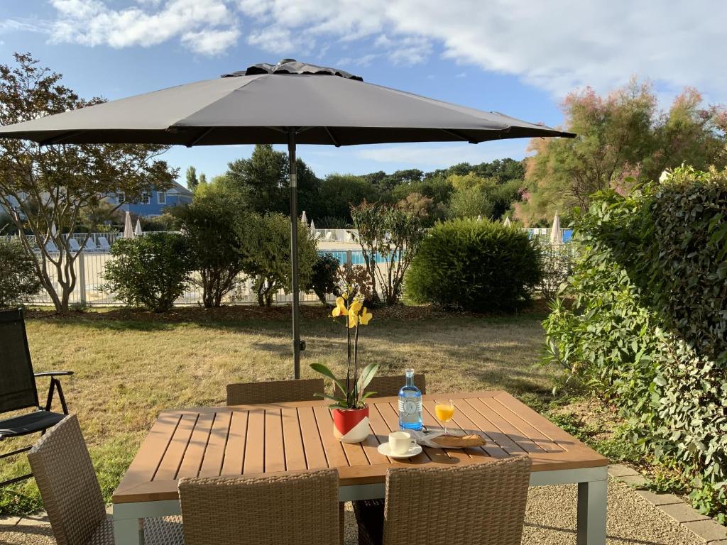 une table en bois avec un parasol dans une cour dans l'établissement LE BOCAGE 38 - Bourgenay - Piscine chauffee, à Saint-Hilaire-de-Talmont