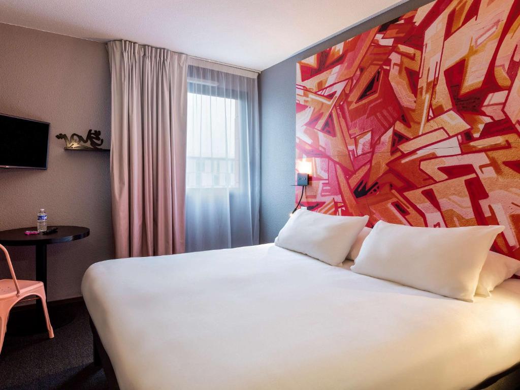 a hotel room with a large white bed with a painting on the wall at Ibis Styles Toulouse Centre Canal du Midi in Toulouse