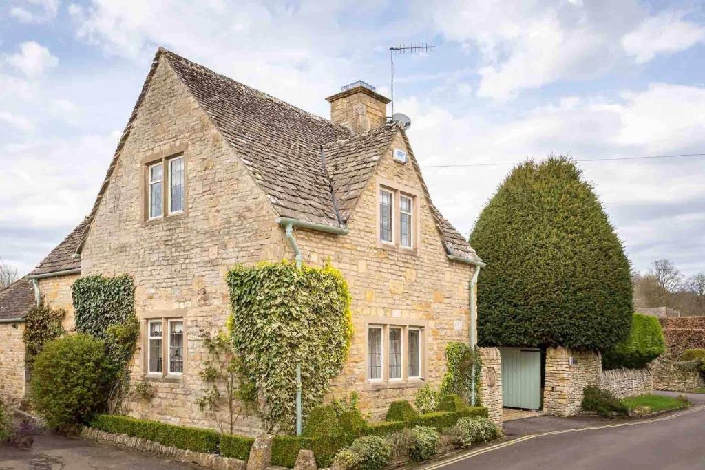 a large stone house with a roof at Mill Stream Cottage in Lower Slaughter