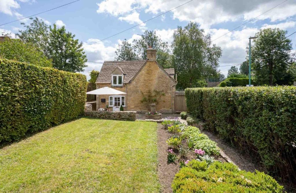 a house with a hedge in front of a yard at Weir Cottage in Bourton on the Water