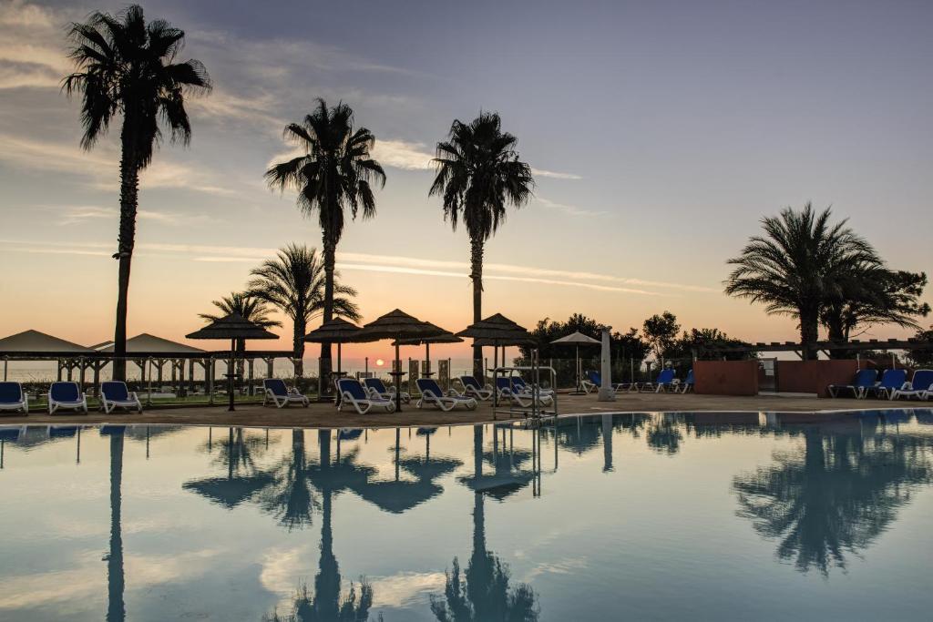 una piscina con palmeras y sillas y una puesta de sol en Belambra Clubs Borgo - Pineto, en Borgo