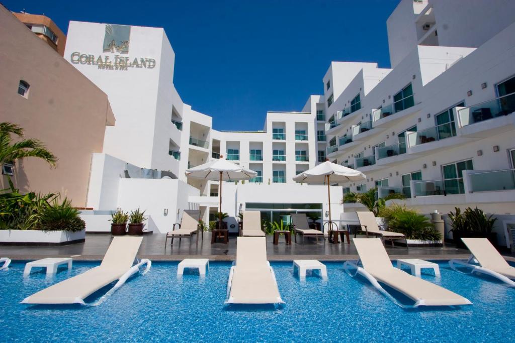 a pool with lounge chairs and umbrellas in front of a building at Coral Island Beach View Hotel in Mazatlán