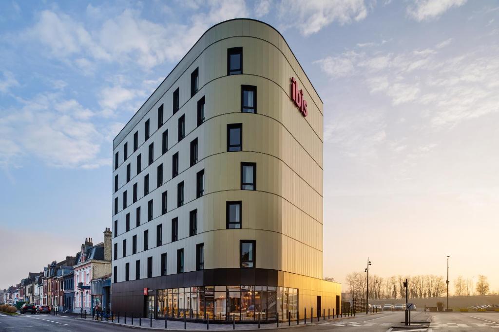 a tall white building with a red sign on it at ibis Bethune Centre Gare in Béthune