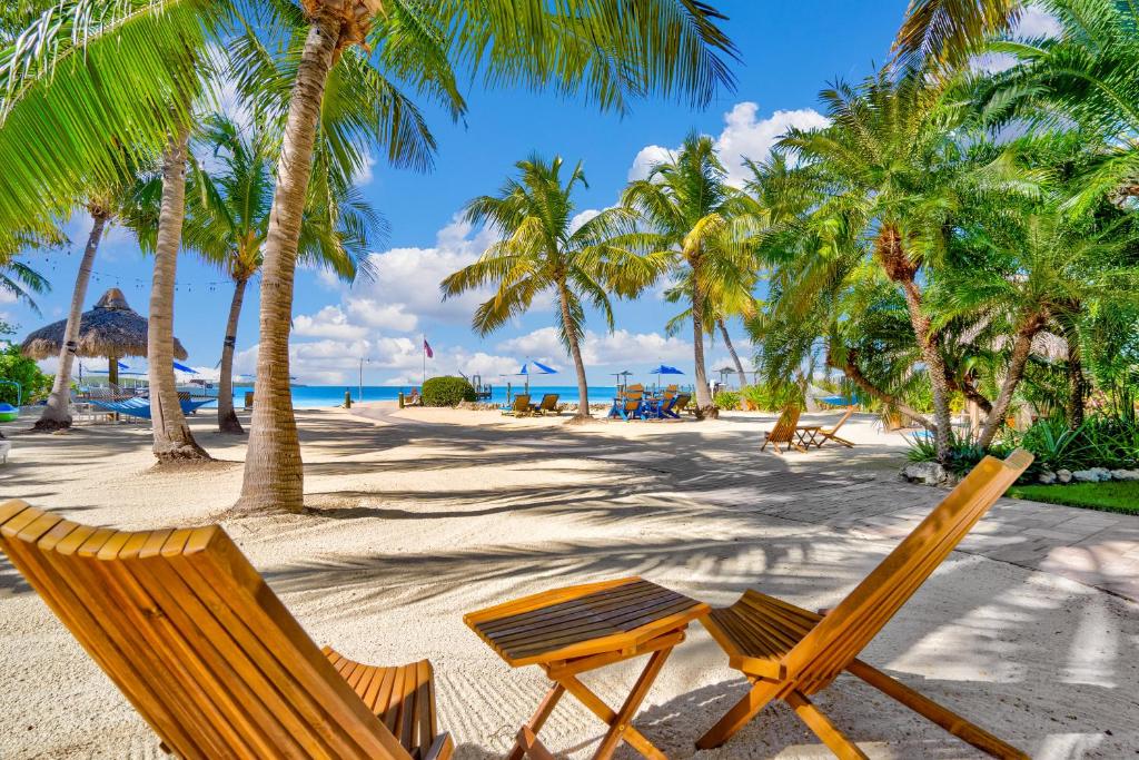 Island Bay Resort في كي لارغو: كرسيين وطاولة على شاطئ به نخيل