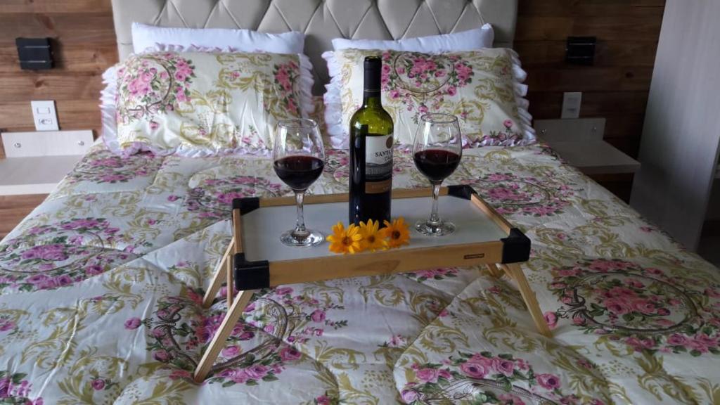 Una botella de vino y dos copas en una cama. en Pousada Sitio Bella Vista en Urupema