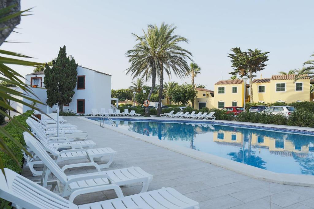 a pool with white lounge chairs next to a building at Aparthotel FLORA PARK & AQUAROCK in Cala en Bosc