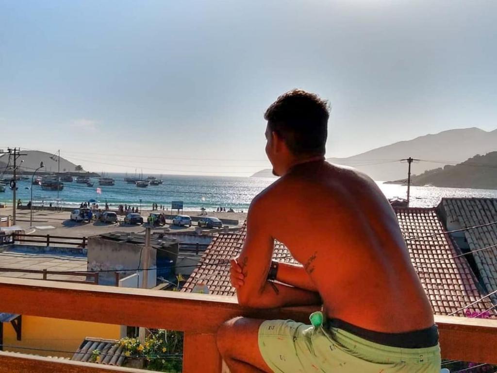 um homem sentado num corrimão olhando para a praia em Enseada Hostel em Arraial do Cabo