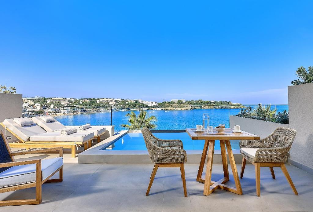 een patio met een tafel en stoelen en uitzicht op het water bij Castello Infinity Suites - Adults Only in Agia Pelagia