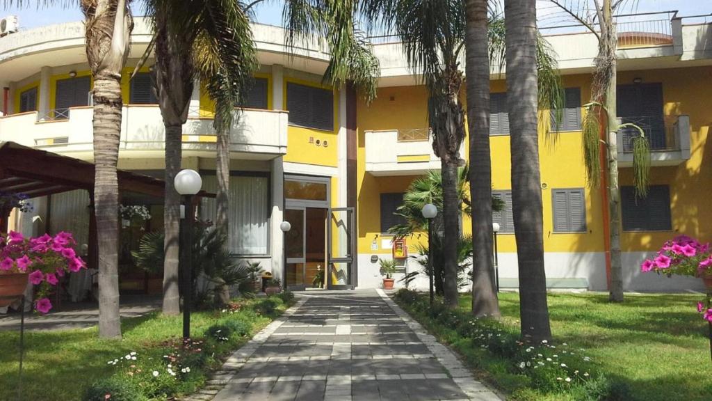 un edificio amarillo con palmeras y una pasarela en Oasi Park Hotel, en Mascali