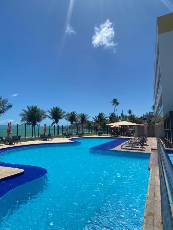 a pool at a resort with blue water and palm trees at Tabatinga Residence Flat Pé na Areia II in Conde
