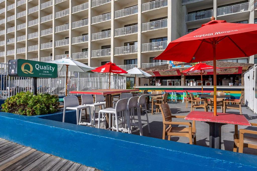 an outdoor patio with tables and chairs and red umbrellas at Quality Inn Boardwalk in Ocean City