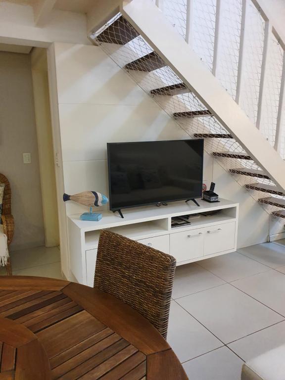a living room with a television on a white dresser under a staircase at Casa- Maresias 3 minutos da praia in Maresias