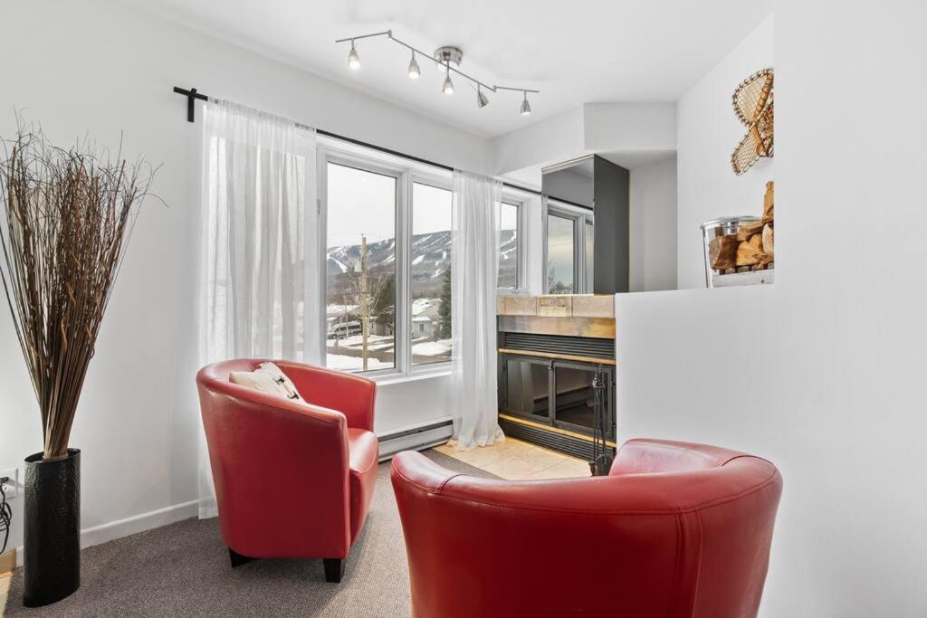 una sala de estar con 2 sillas rojas y una ventana en INITIAL - LE REPOS DES SKIEURS - Mont-Sainte-Anne en Saint-Férréol-les-Neiges
