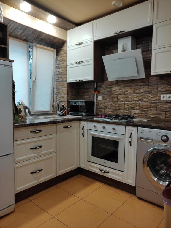 a kitchen with white cabinets and a washer and dryer at Comfortable Apartment in Kremenchuk