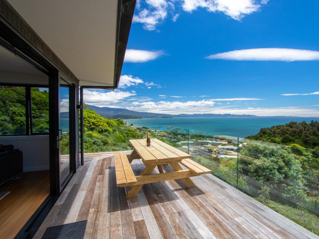 a wooden picnic table on a deck with a view of the ocean at Bay Vista Beauty - Pōhara Holiday Home in Pohara