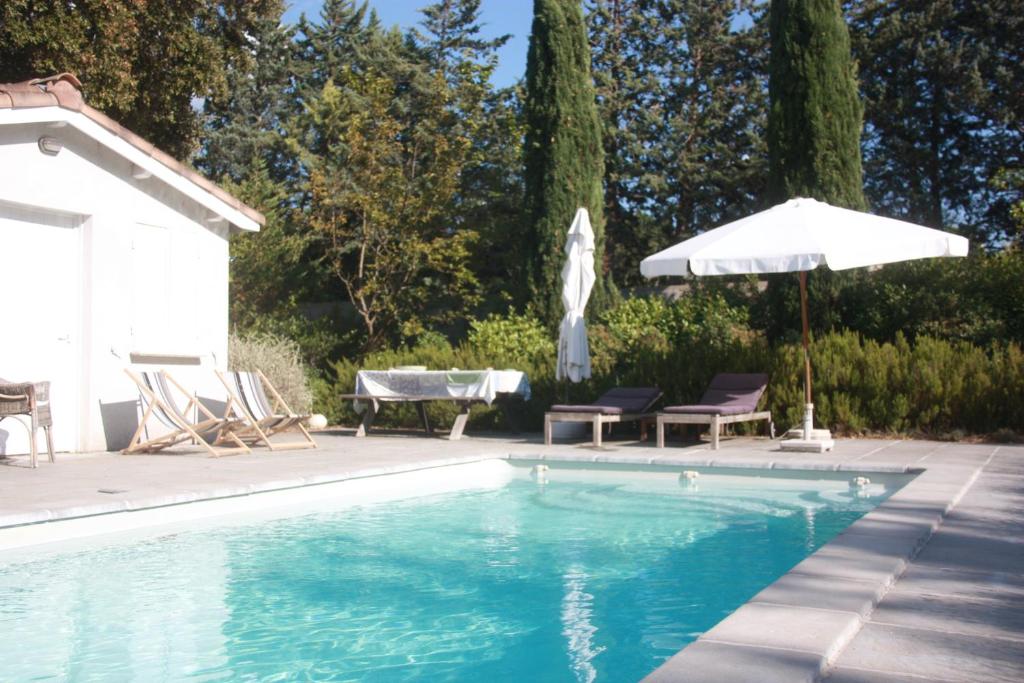 uma piscina com um guarda-sol e cadeiras e uma mesa em Au Coin des Cerisiers em Montclus