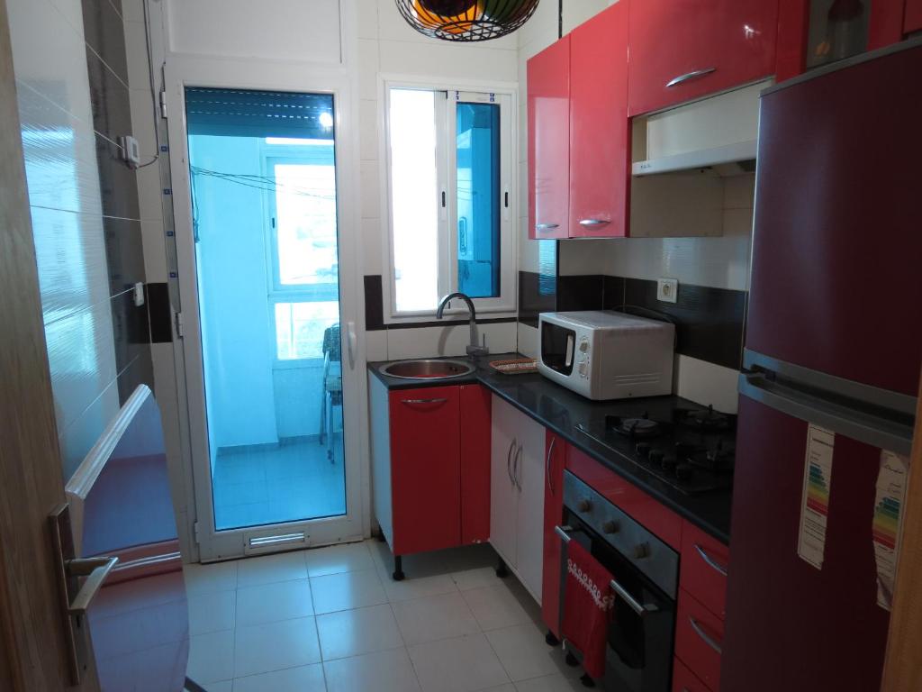 a small kitchen with red cabinets and a microwave at Beautiful appartment with a glorious sea view in Monastir