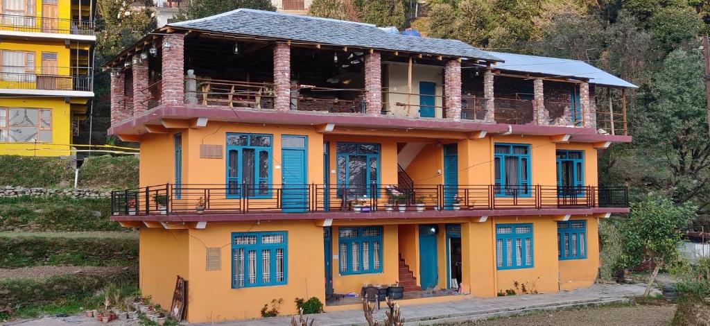 a yellow house with blue doors and a balcony at White Rabbit Guest House in Dharamshala