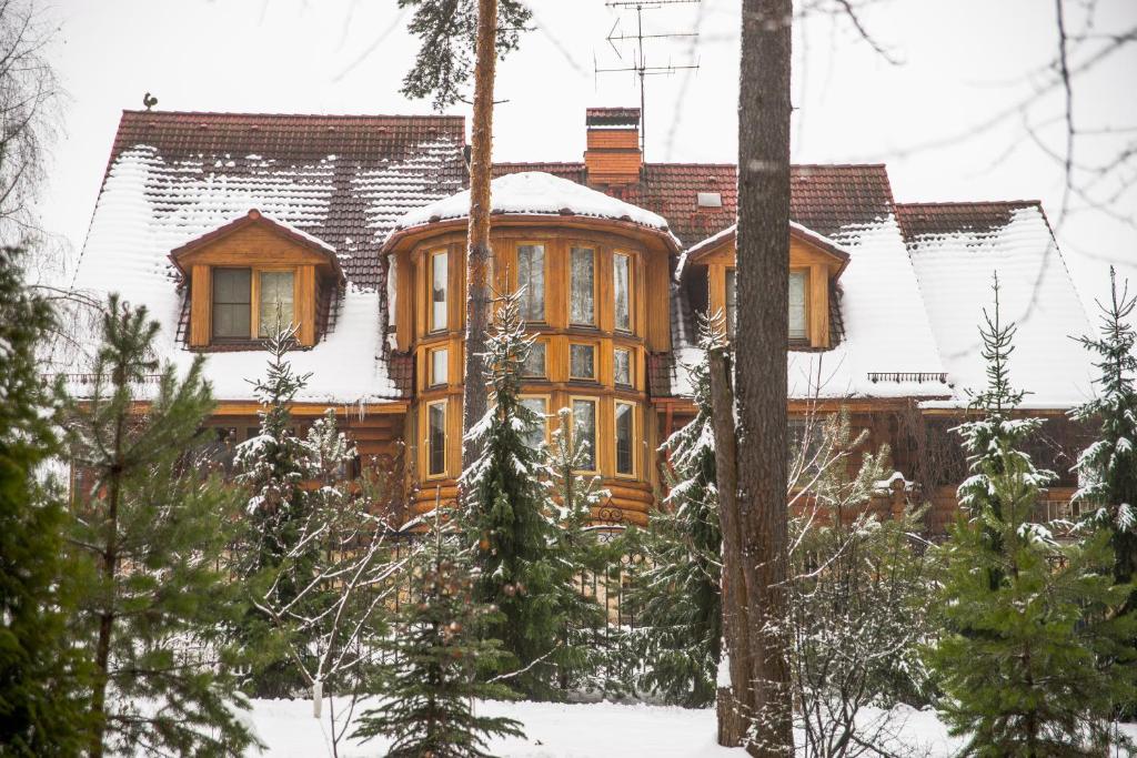 a wooden house in the snow with trees at Ulitkino Park Hotel in Rayki
