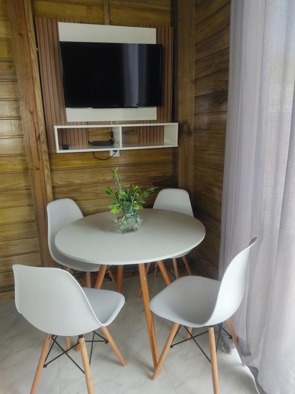 uma mesa branca com quatro cadeiras e uma televisão em Chalés Costa Esmeralda, Bombinhas em Bombinhas