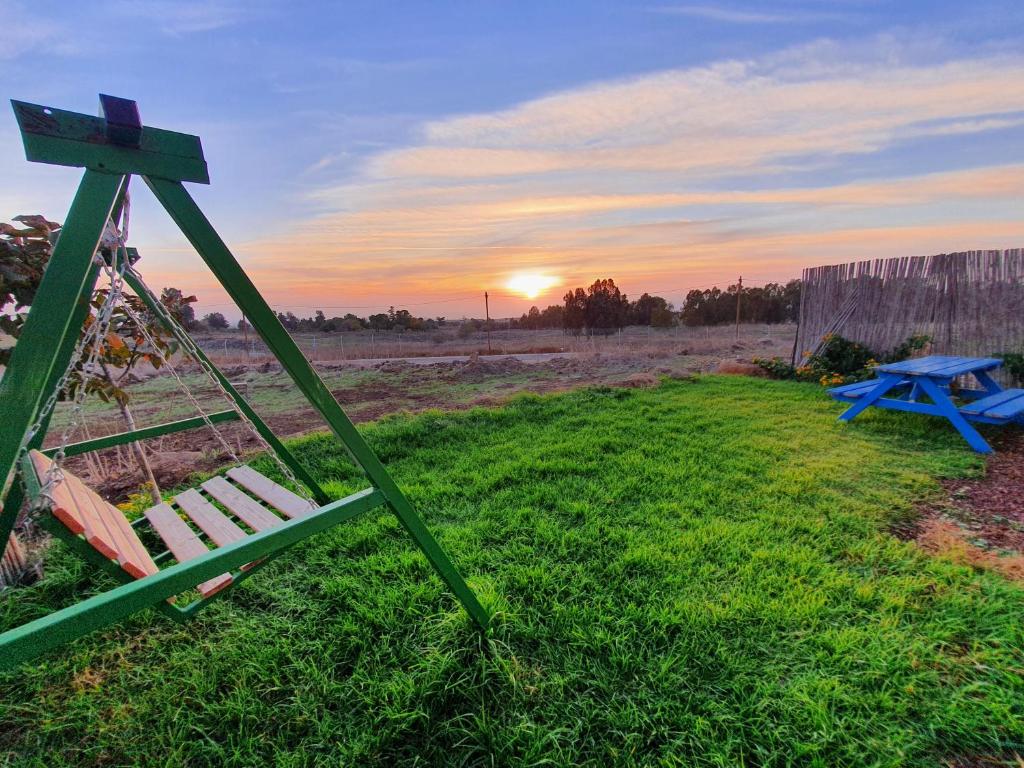 um banco e uma mesa de piquenique num campo com o pôr-do-sol em קשת לכנרת-יחידת הקרקע em Keshet