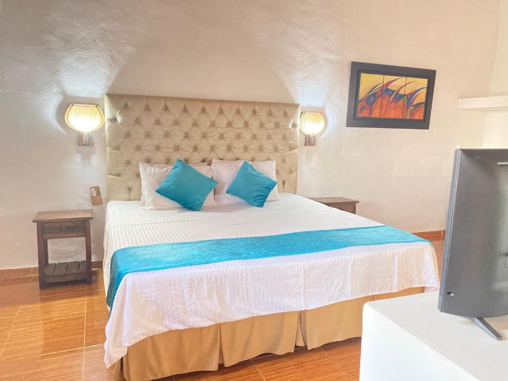 1 dormitorio con 1 cama con almohadas azules y TV en Hotel Y Spa Santos De Piedra, en Barichara