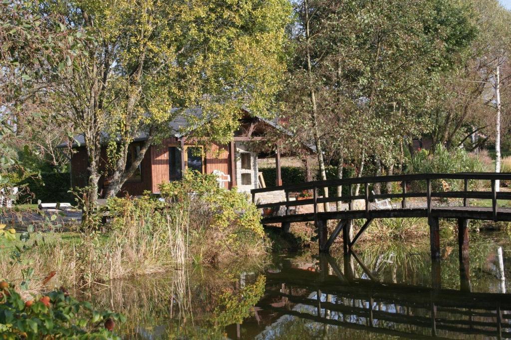 eine Holzbrücke über einen Wasserkörper mit einem Haus in der Unterkunft Le Chalet Pré de la Fontaine in Paliseul