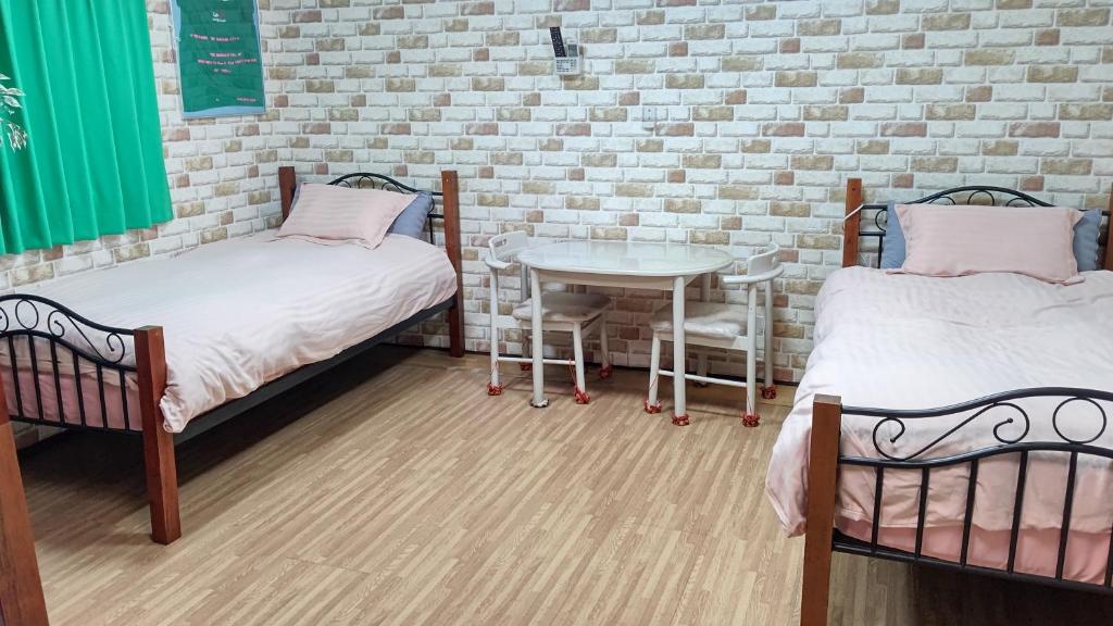 duas camas e uma mesa num quarto com uma parede de tijolos em HILDA INN em Kashiwa