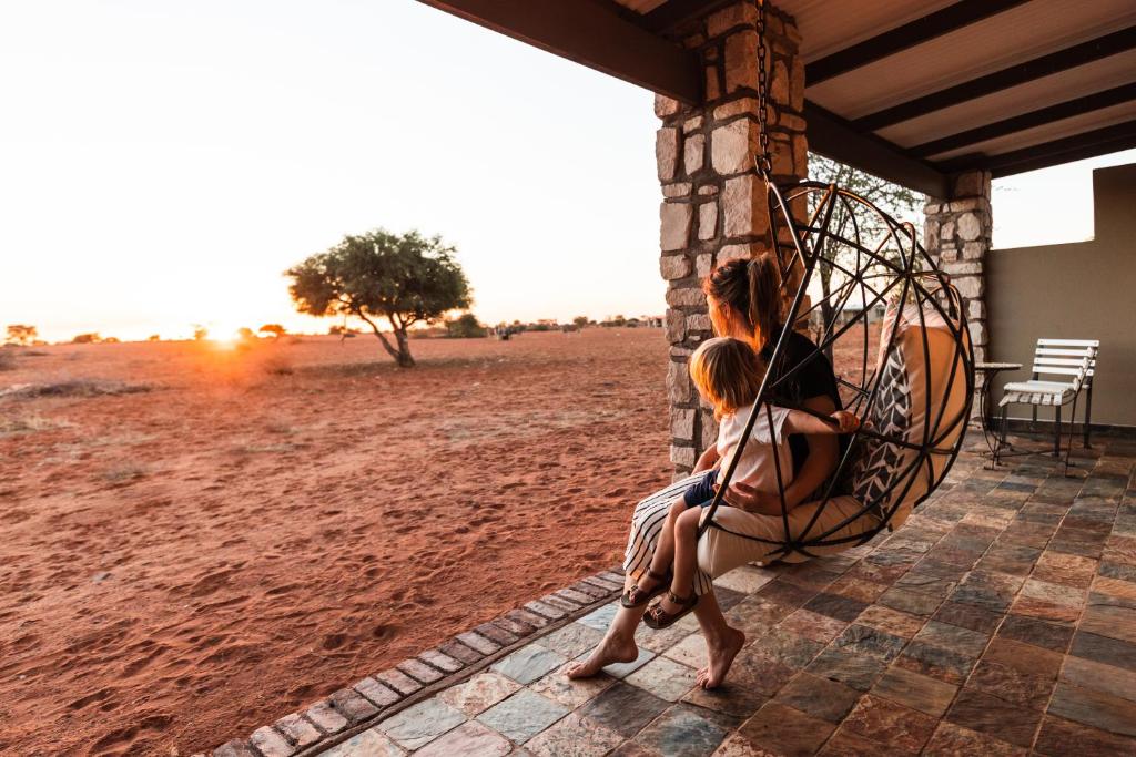 Eine Frau und ein Kind sitzen auf einer Veranda mit einem Regenschirm in der Unterkunft Gondwana Kalahari Anib Lodge in Hardap