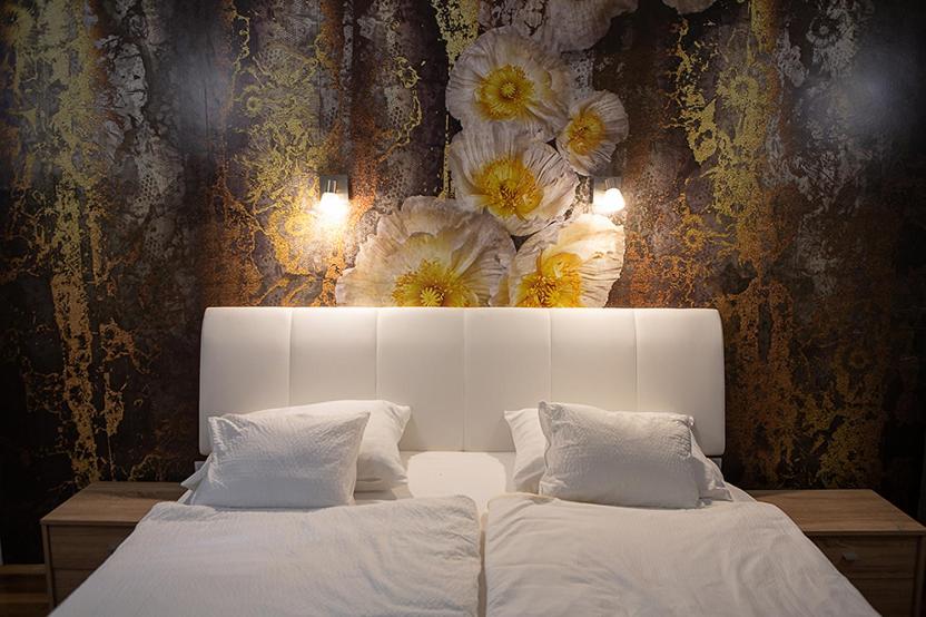 1 dormitorio con 1 cama blanca con flores en la pared en V8-Kelemen Panzió en Makó