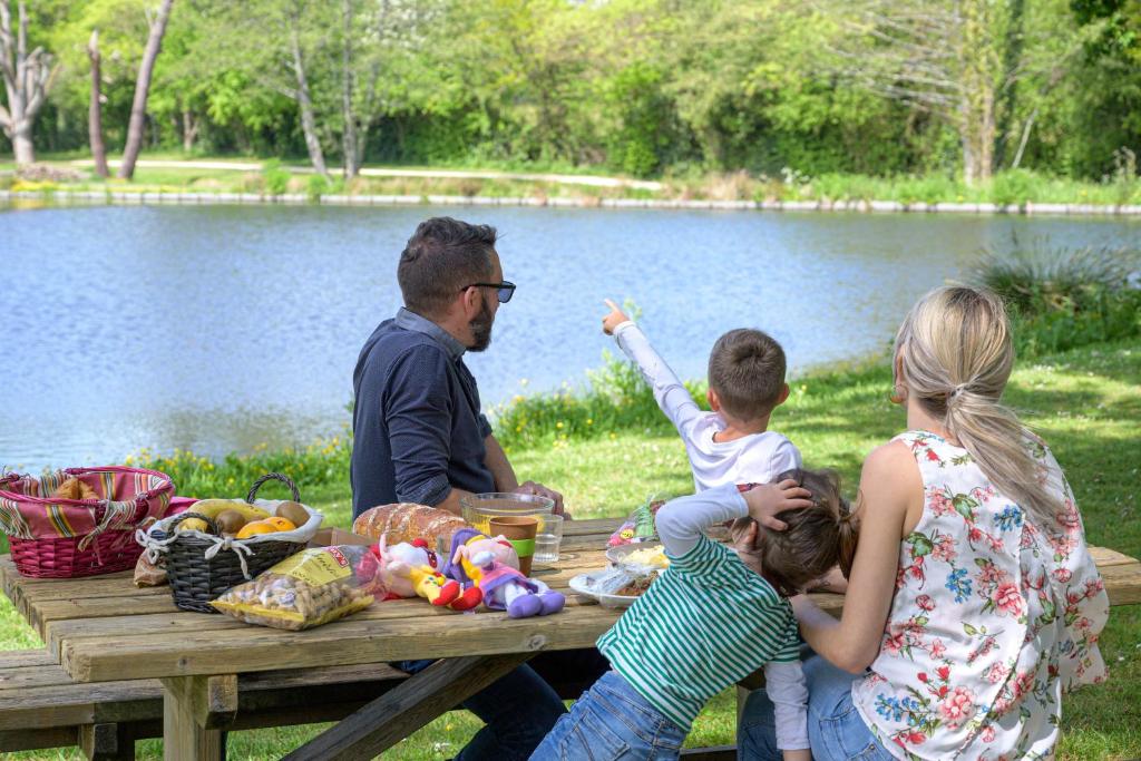 a family sitting at a picnic table near a lake at Camping Capfun La Bretèche in Les Épesses