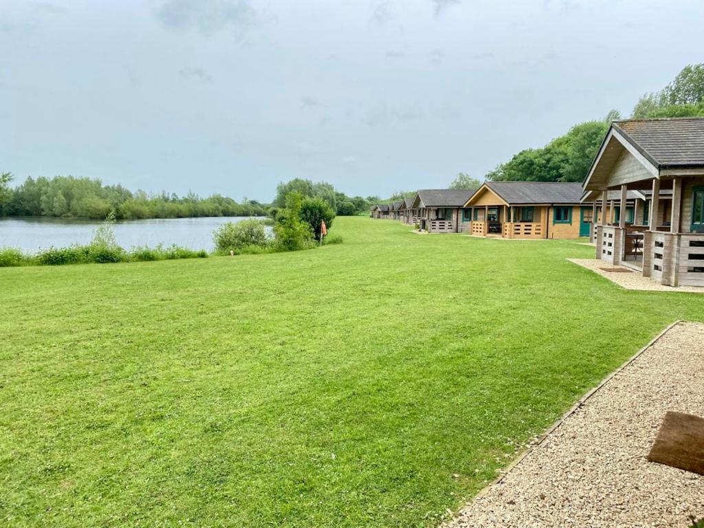 a large grassy field next to a row of cottages at Tufty Lodge, Lake Pochard lodge 9 in South Cerney