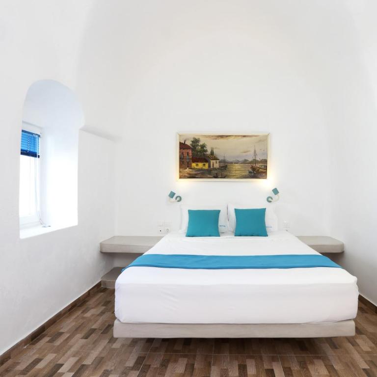 biała sypialnia z białym łóżkiem z niebieskimi poduszkami w obiekcie Church and Cave - Santorini Private Residences w mieście Mesaria
