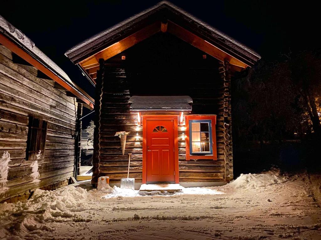 una piccola cabina con una porta rossa nella neve di The Fryksås Chamber a Orsa
