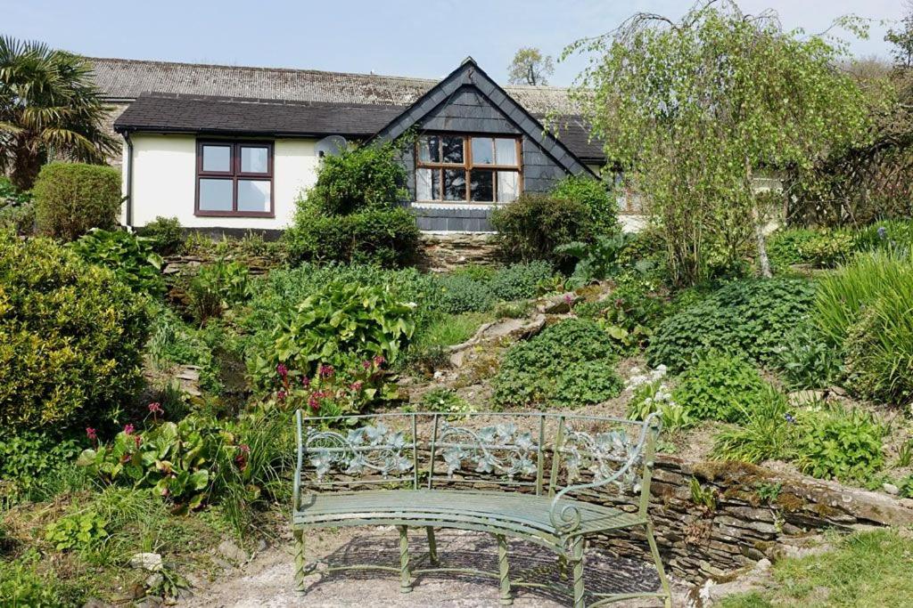 a green bench sitting in the garden in front of a house at Greenswood Cottage - Cosy cottage, rural location, beautiful landscaped gardens with pond and lake in Dartmouth