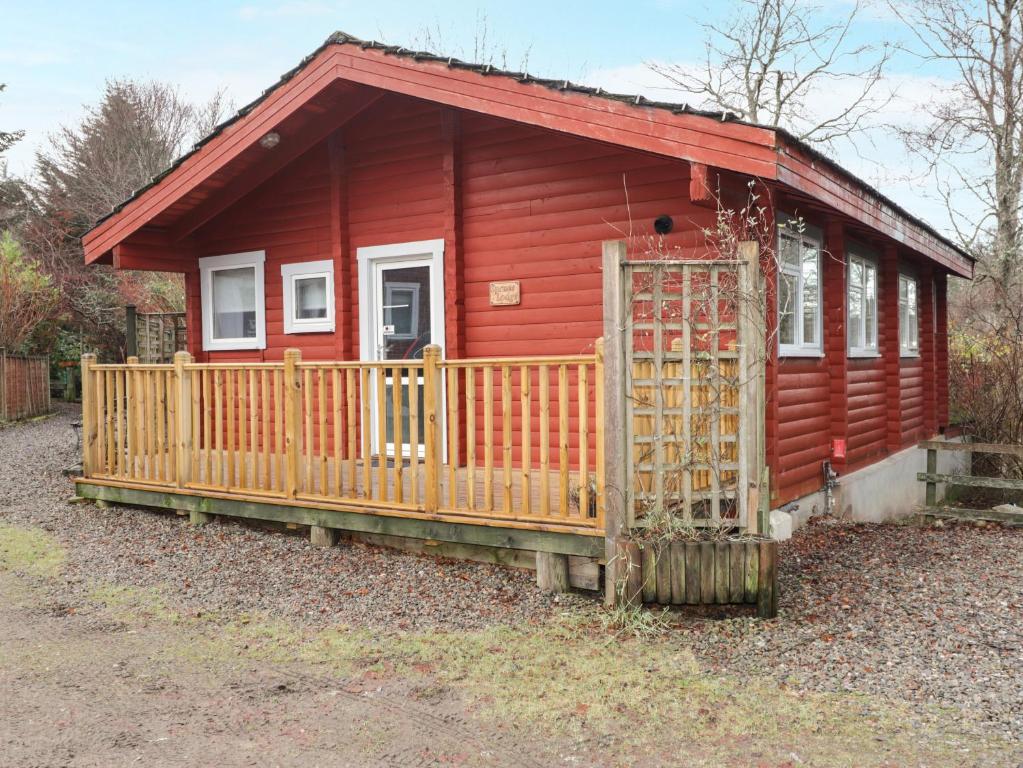 a red cabin with a wooden gate in front of it at Spruce Lodge in Strathpeffer