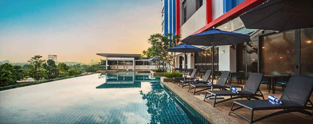 a pool with chairs and umbrellas next to a building at Sunway Hotel Big Box in Nusajaya