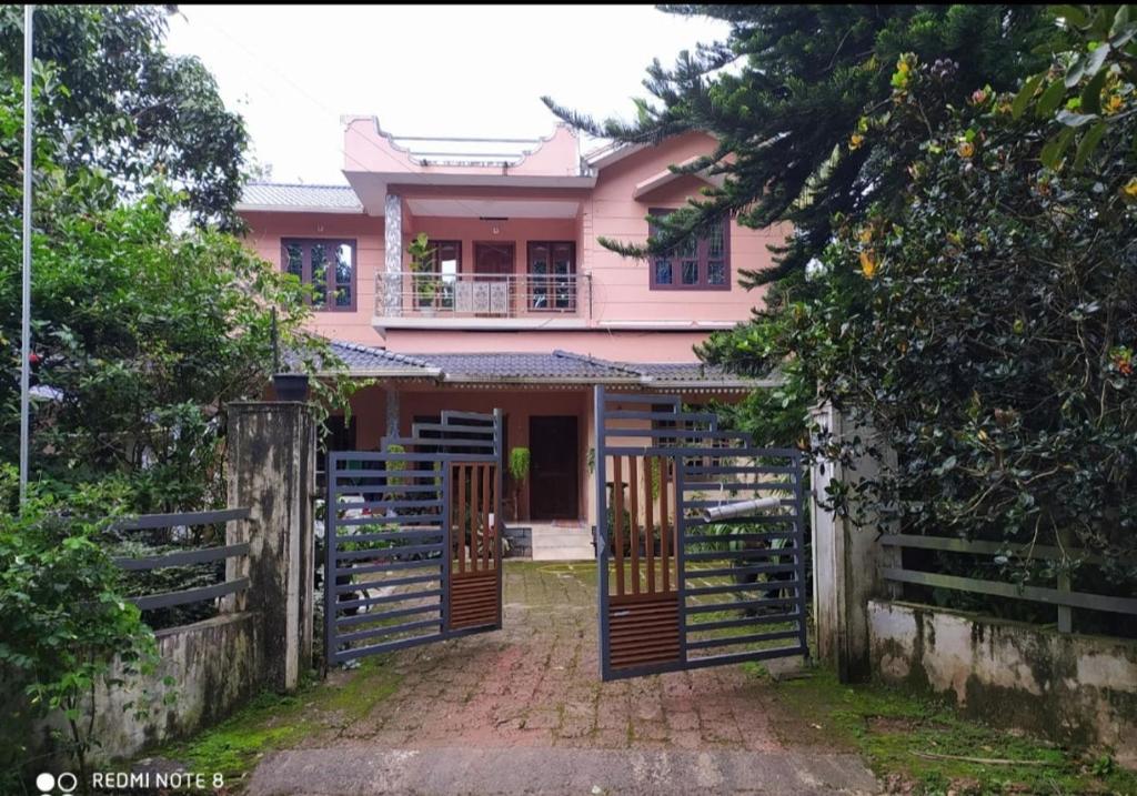 Puzhayoram home stay, Palakkuli, Mananthavadi wayanad kerala في مانانثافادي: منزل وردي مع بوابة وسياج