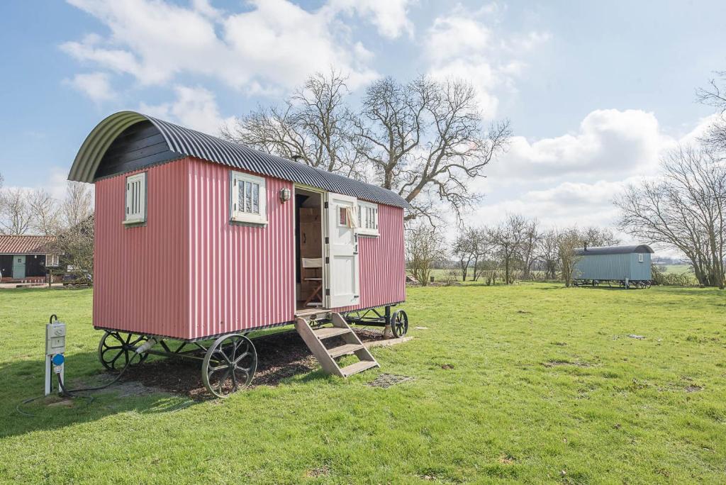 a small red house with a black roof in a field at Thyme Shepherds Hut Boundary Farm Air Manage Suffolk in Woodbridge