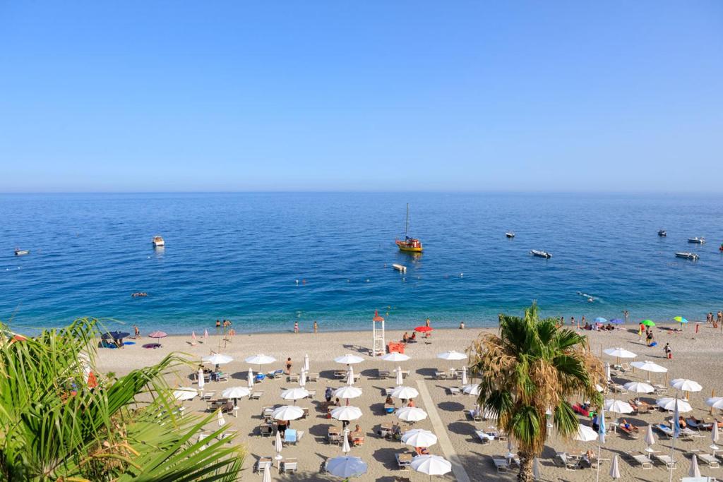 a beach with umbrellas and people swimming in the ocean at Albatros Beach Hotel in Letojanni