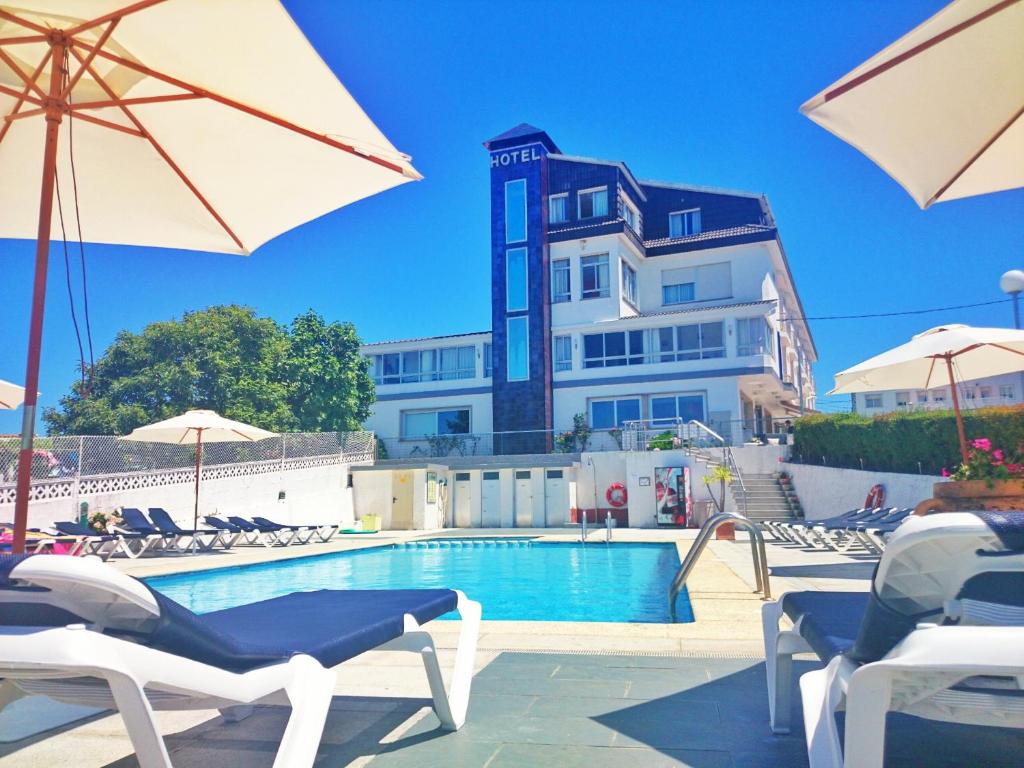 einem Pool mit Stühlen und Sonnenschirmen vor einem Gebäude in der Unterkunft Hotel Marola in A Lanzada