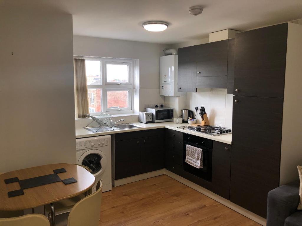 een keuken met zwarte kasten en een tafel en een wastafel bij 2nd Floor Town Centre Apt with FREE Parking in Loughborough