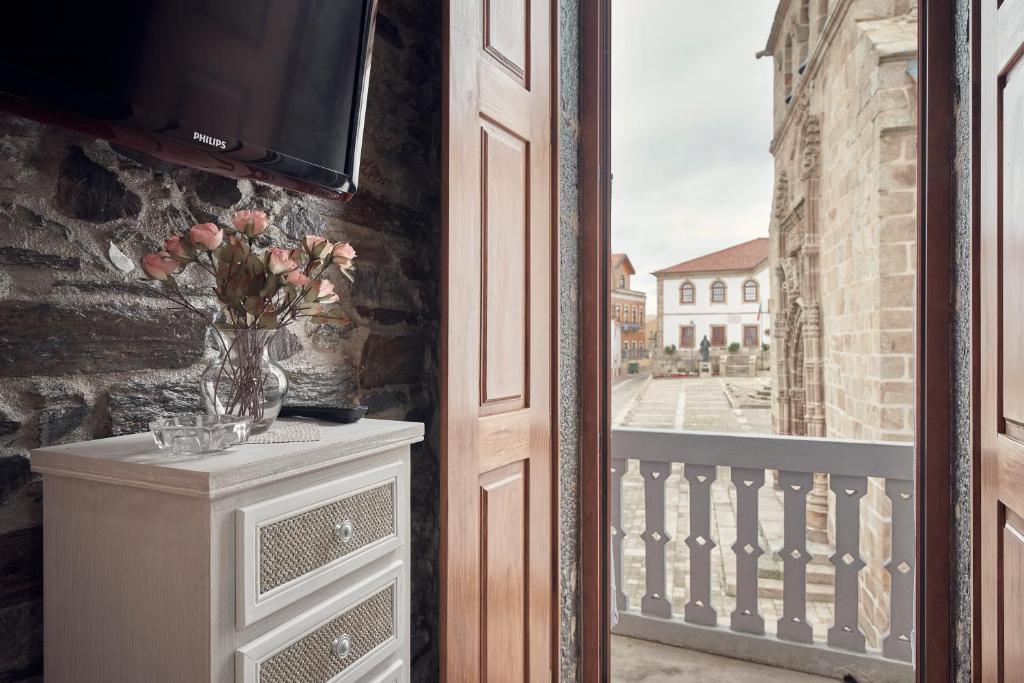 un jarrón de flores en un tocador junto a una ventana en Casa do Largo da Igreja en Vila Nova de Foz Coa